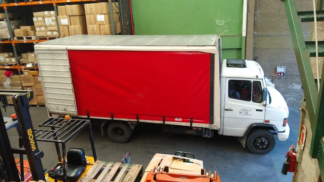 Camión con caja de lona cargando junto a los racks del depósito